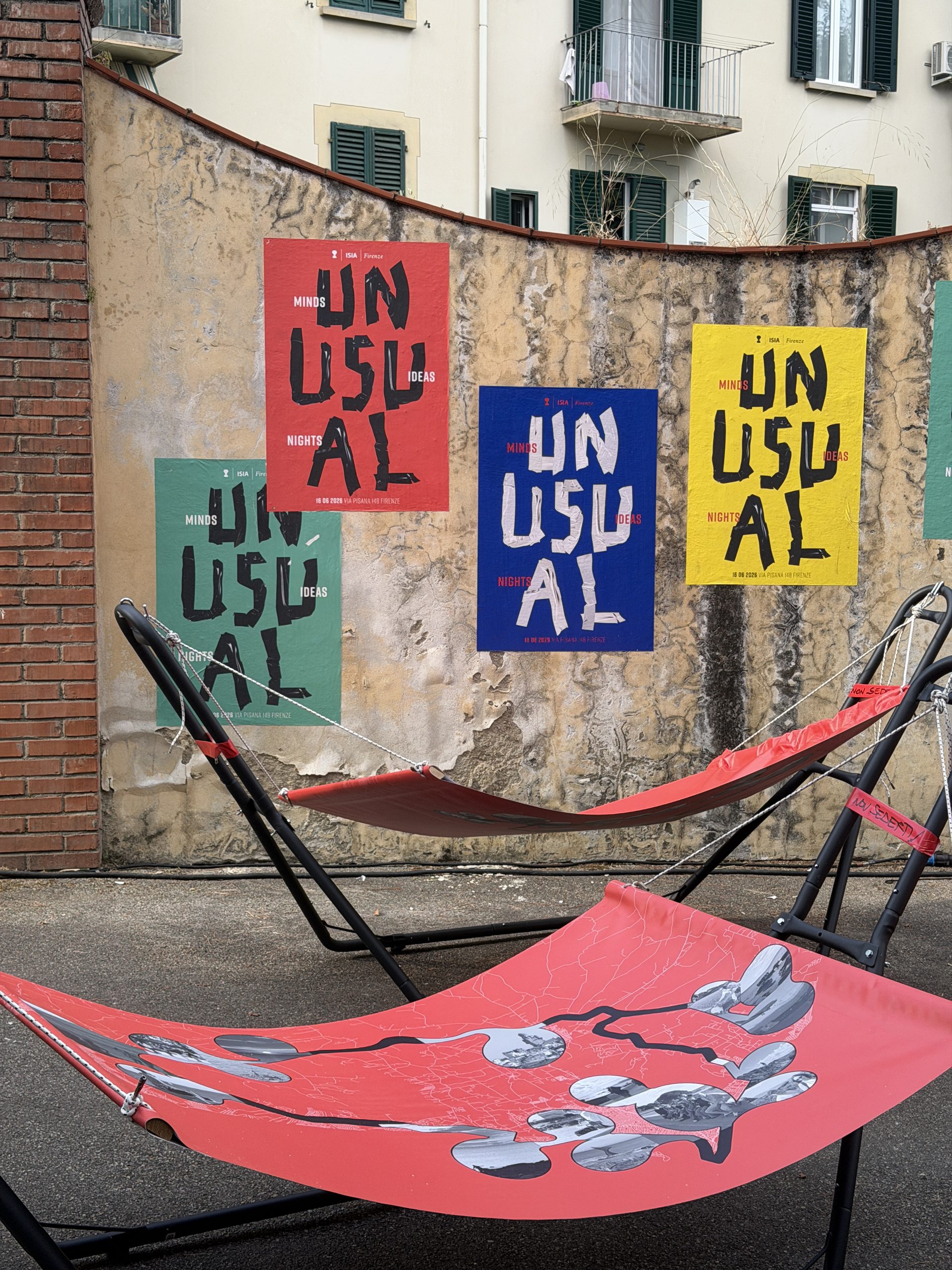 A red hammock printed with the map and bubble-shaped photos, behind it the peeling wall with red, blue, yellow and green Unusual posters.