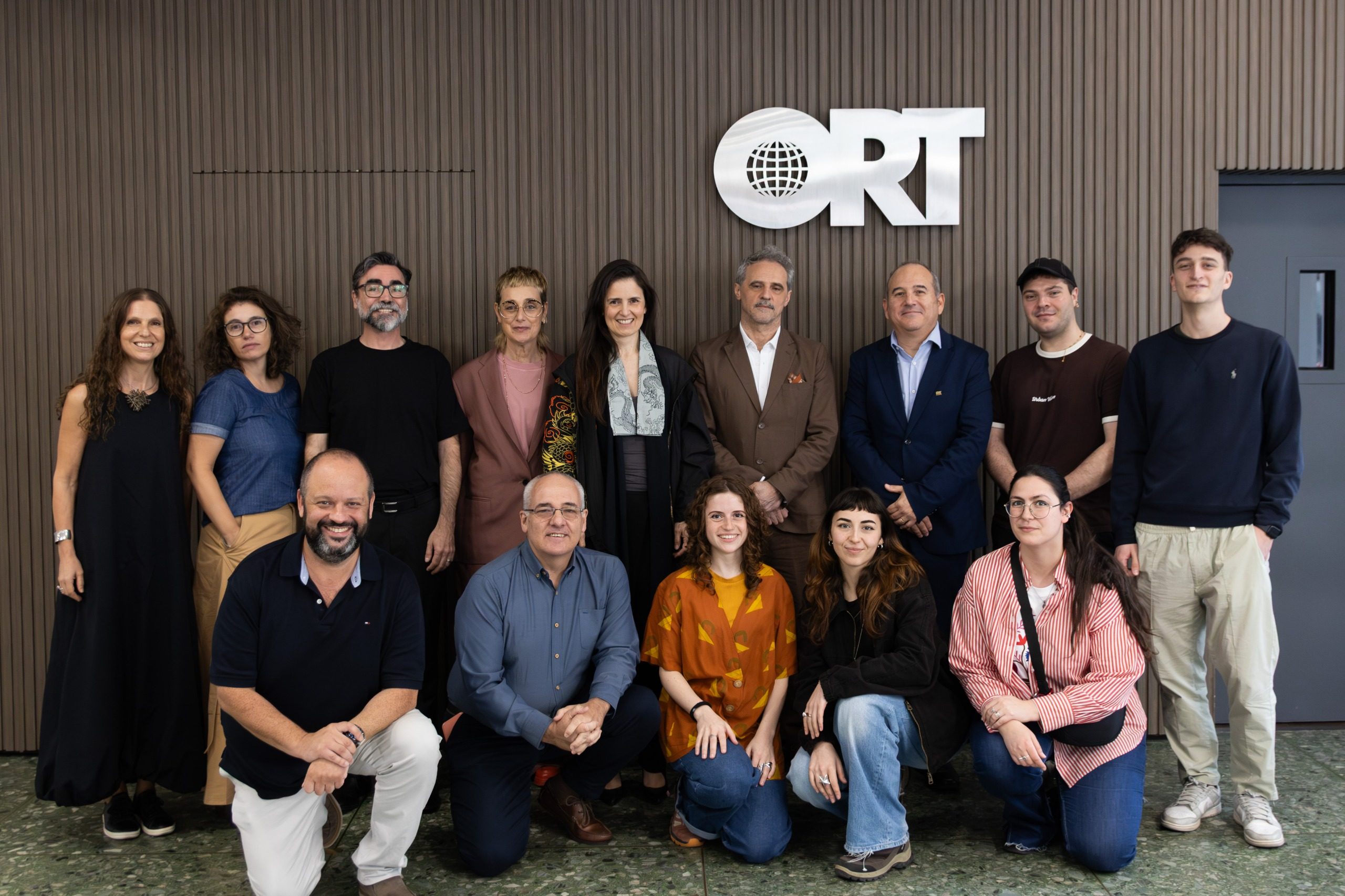 Group photo at Universidad ORT, Montevideo: the ISIA Firenze delegation and the ORT team, standing and crouching, in front of the wooden wall with the ORT logo.