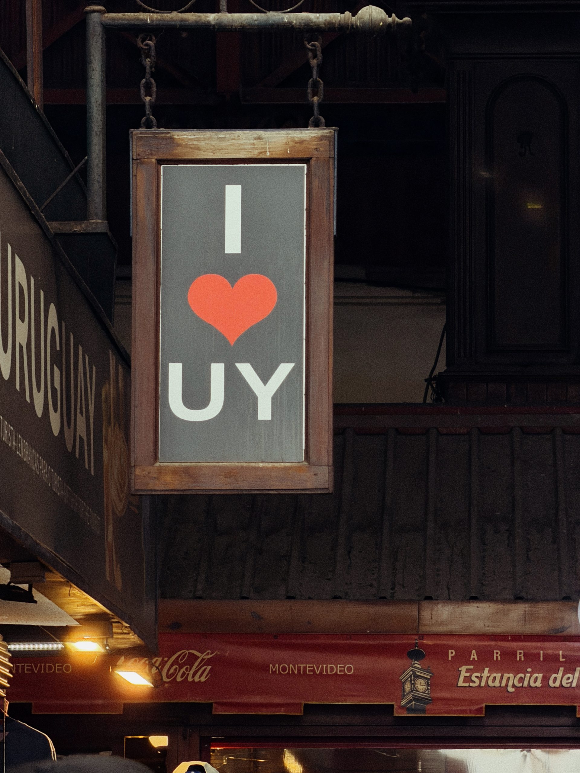 At the Mercado del Puerto: a hanging sign reading I ♥ UY, under the red signs of the parrillas.