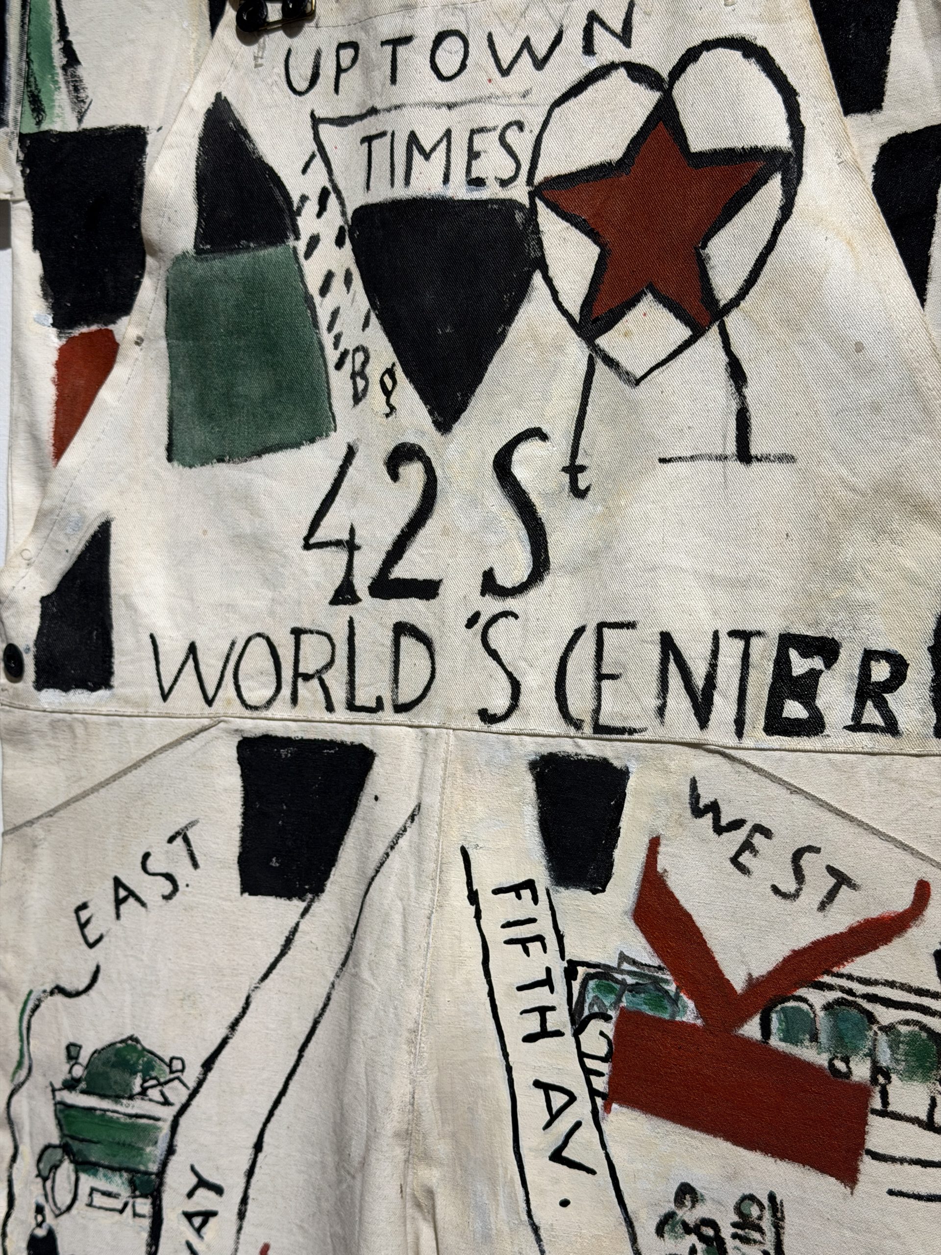 At the Torres García Museum: detail of a work painted on raw canvas, with the words Uptown Times, 42 St, World’s Center, East, West and Fifth Av among black and green shapes and a red star.