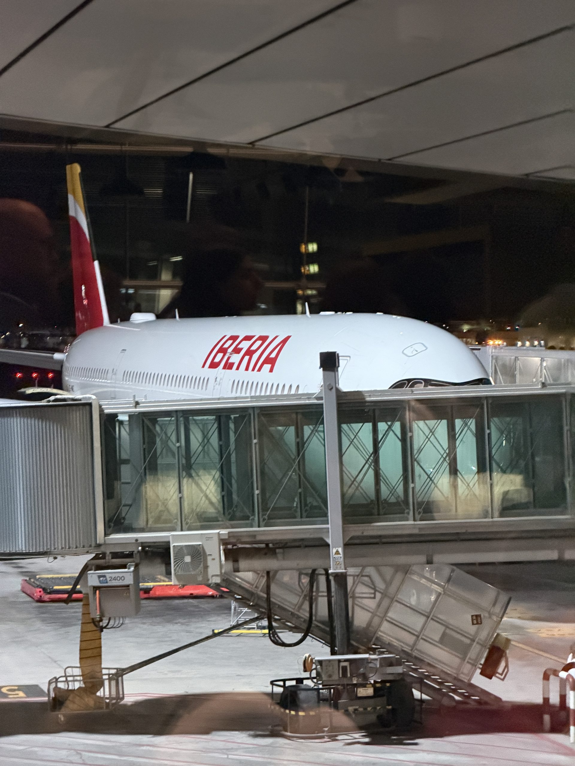 At night, at the Madrid stopover: through the gate window, the white Iberia plane with its red and yellow tail attached to the jet bridge, before the flight to Montevideo.
