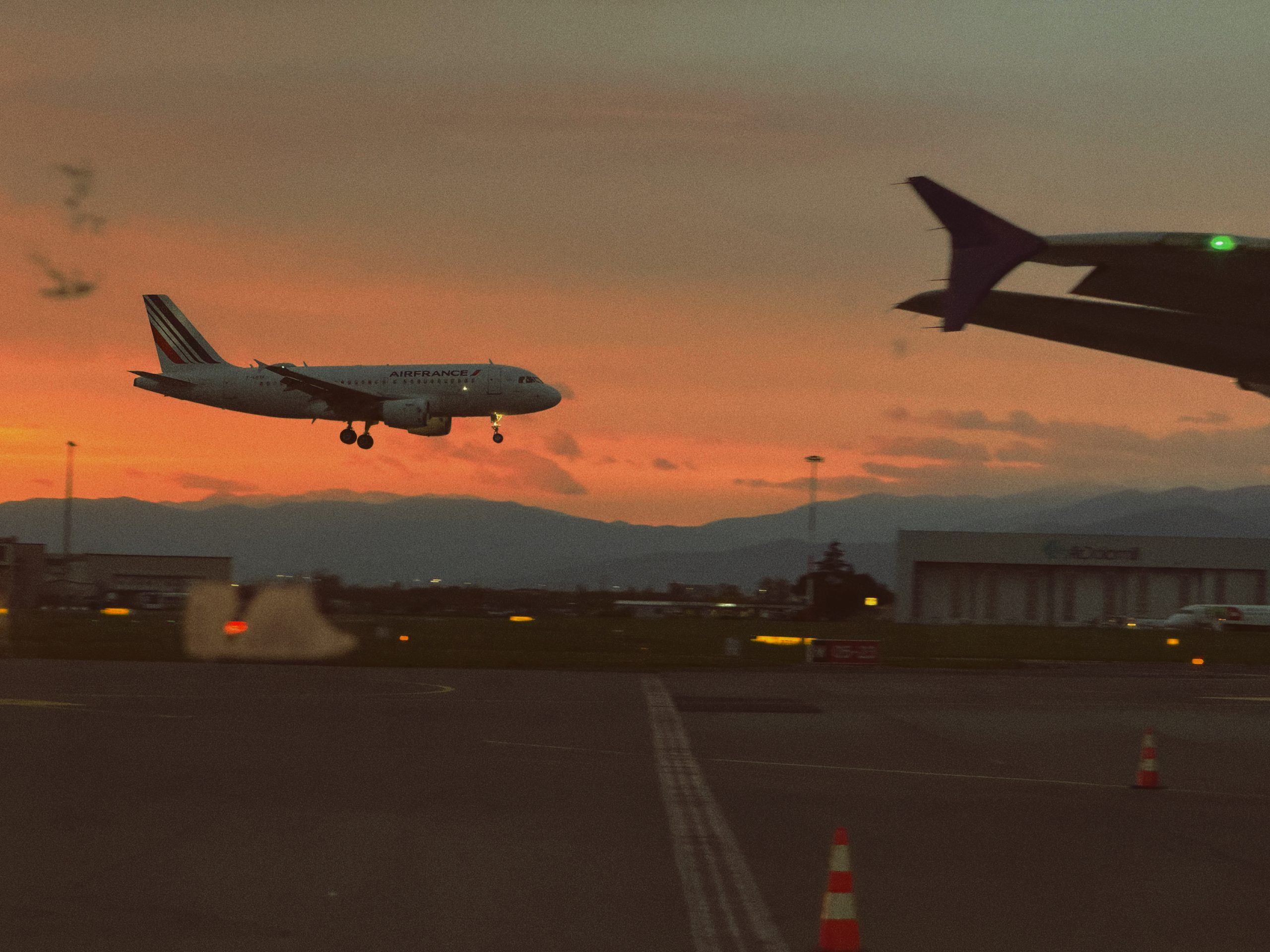 Back in Florence at sunset: an Air France plane landing against an orange sky, dark hills behind, and our plane’s wing in the foreground.