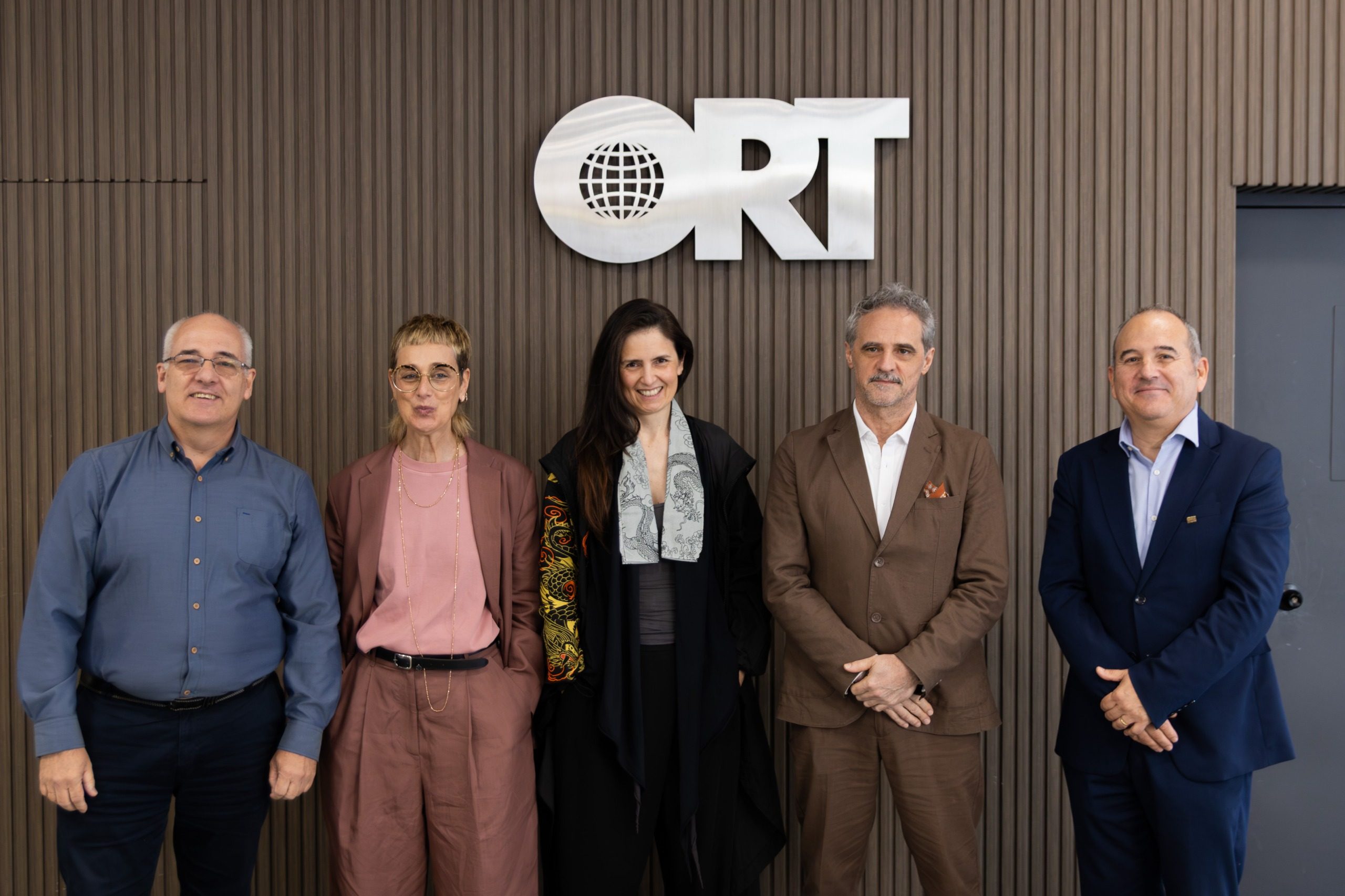 Five people standing in front of the ORT logo on the wooden wall of Universidad ORT Uruguay in Montevideo.